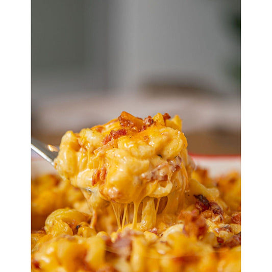 A spoon lifting a dish of bacon mac and cheese, a delectable combination of macaroni, cheese, and bacon.