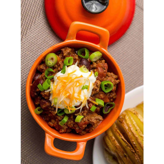 A bowl of Firehouse Chili topped with sour cream and onions in an orange bowl.