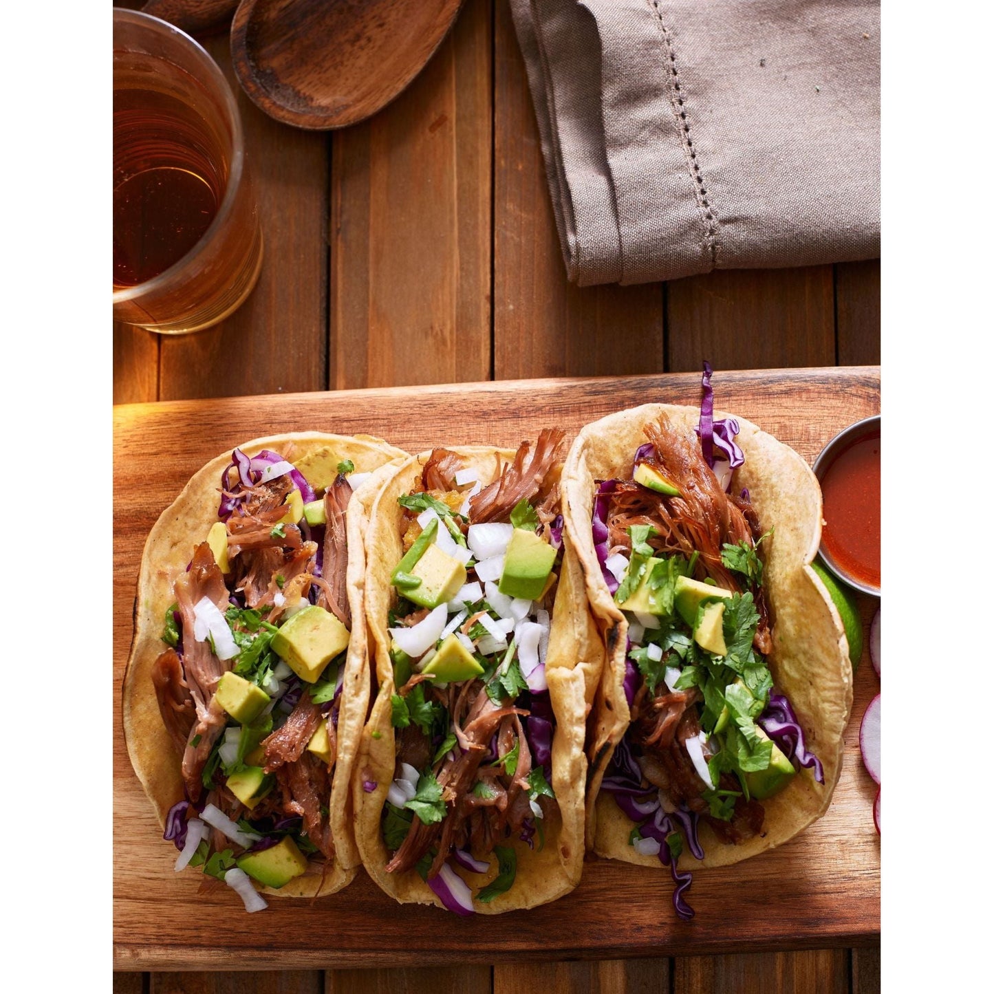 Three delicious tacos with pork, avocado, and cabbage, beautifully presented on a wooden cutting board.